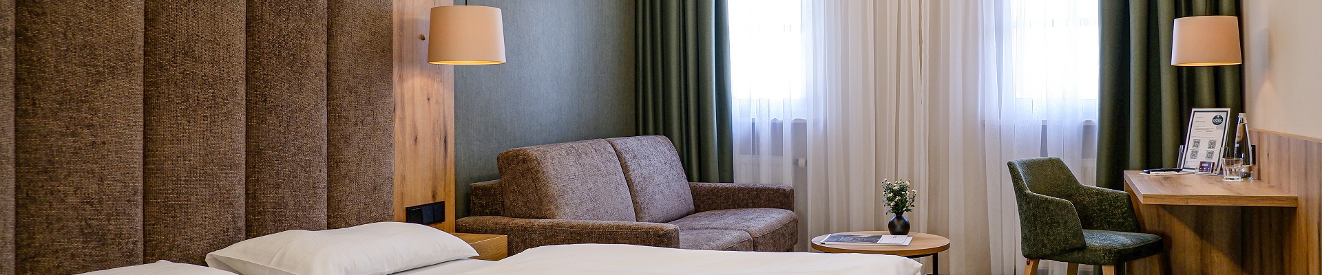 Deluxezimmer für zwei Personen mit Sofa, Schreibtisch und Vorhängen zum verdunkeln.